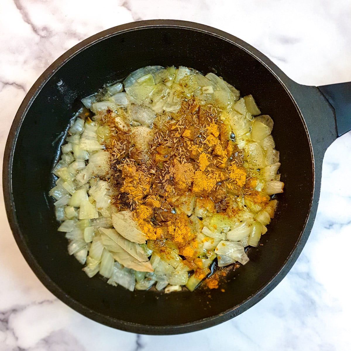 Spices on top of onions in a frying pan.