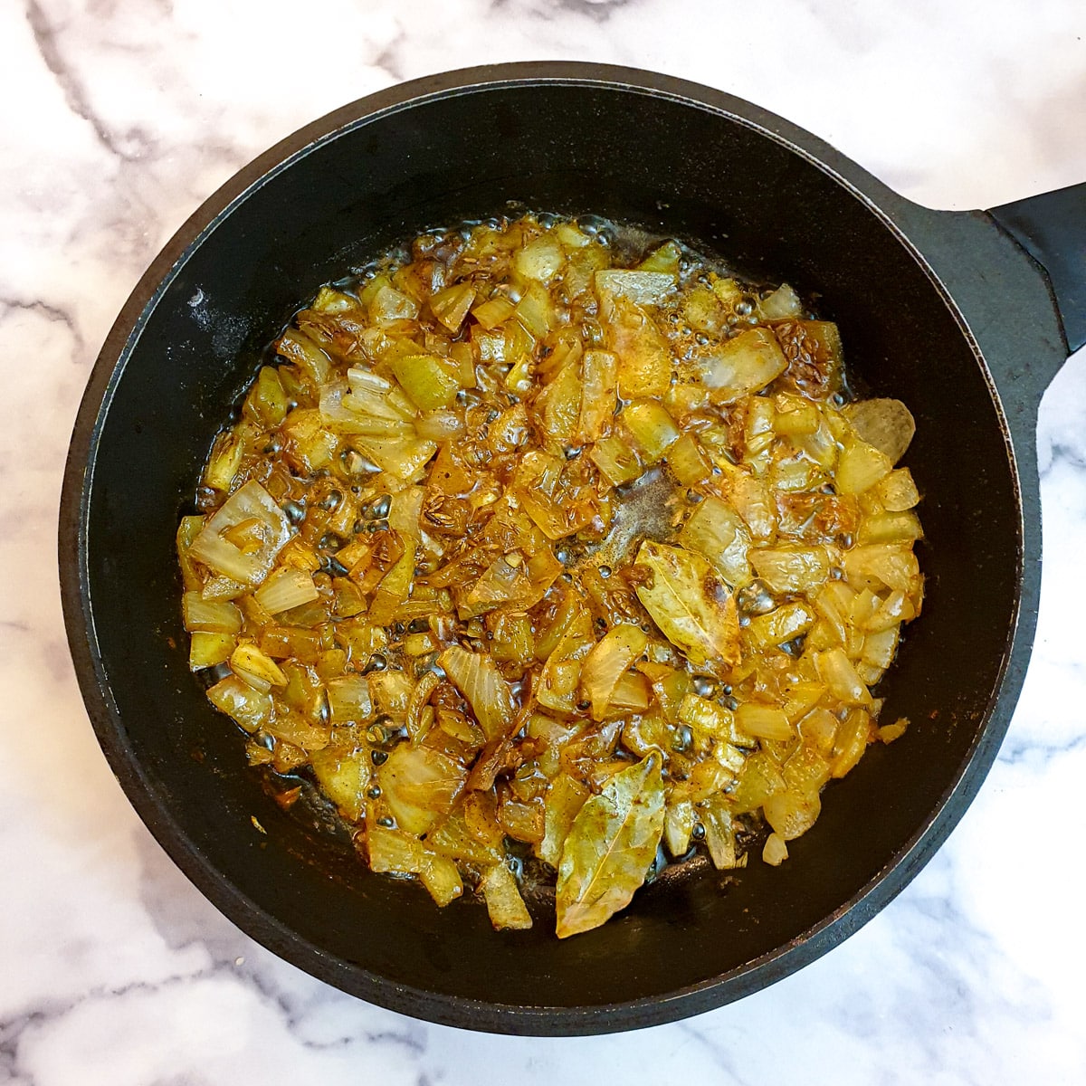 Spices frying with onions in a black frying pan.