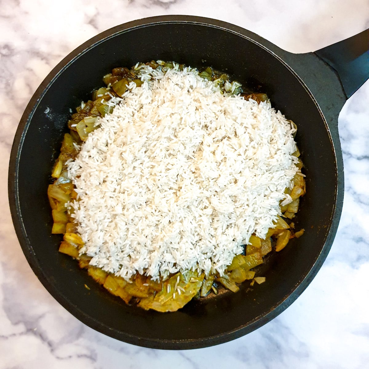 A pile of white rice on top of onions in a frying pan.