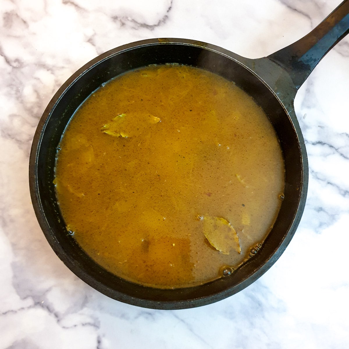 Vegetable stock mixed with the pilau rice ingredients in a frying pan.