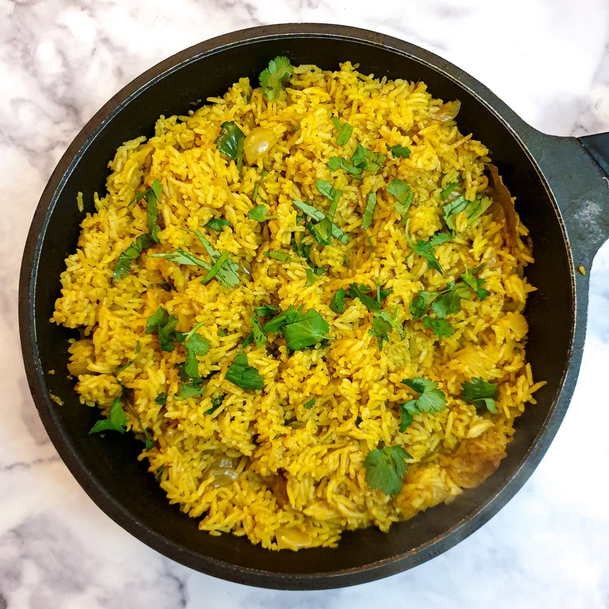 A black frying pan filled with cooked pilau rice and garnished with chopped coriander.