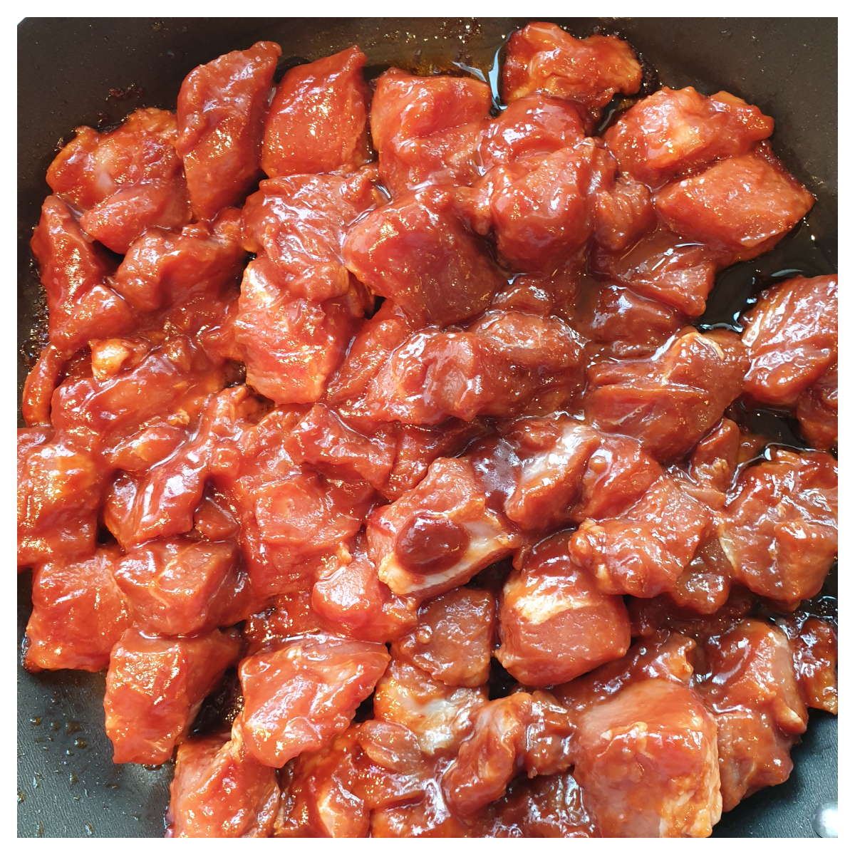 Marinated fresh pork cubes in a frying pan.