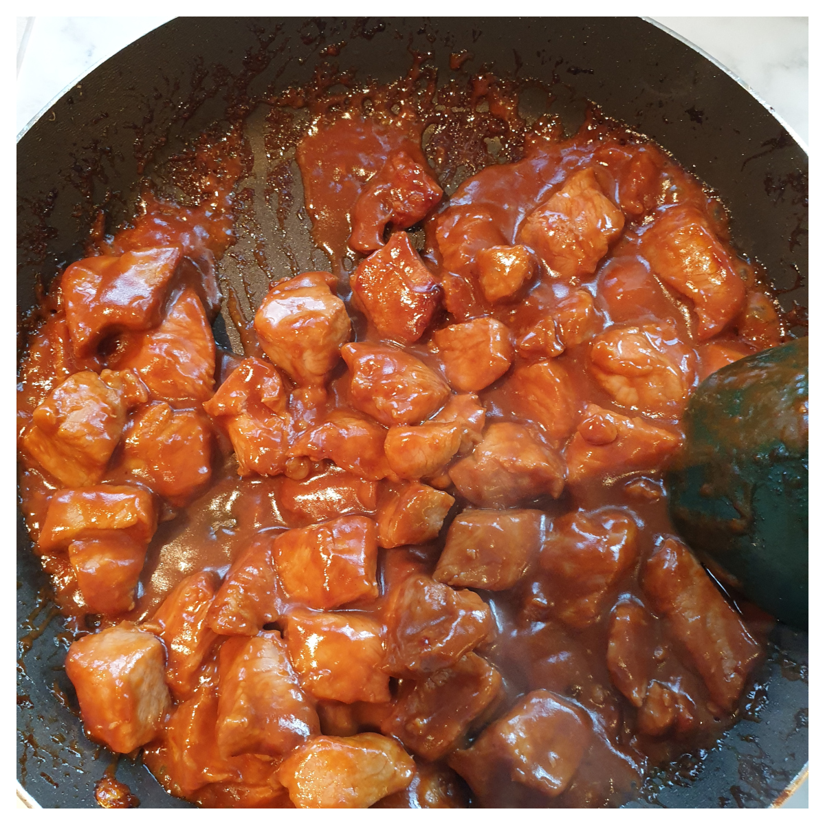 Marinate fresh pork cubes being stir-fried in a frying pan.