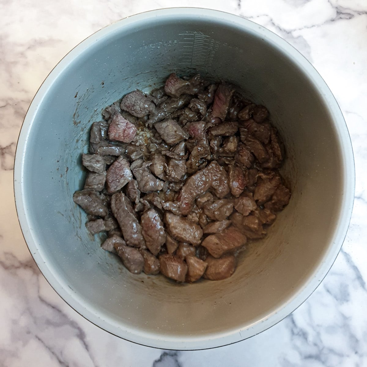 Pieces of beef being browned in a pressure cooker.