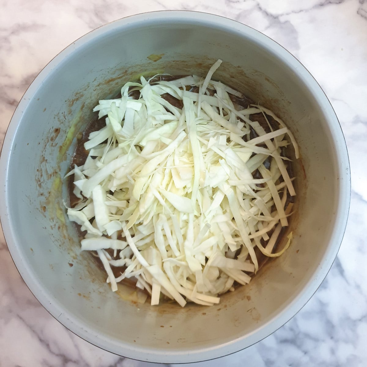 A pile of shredded raw cabbage on top of beef stew in a pressure cooker.