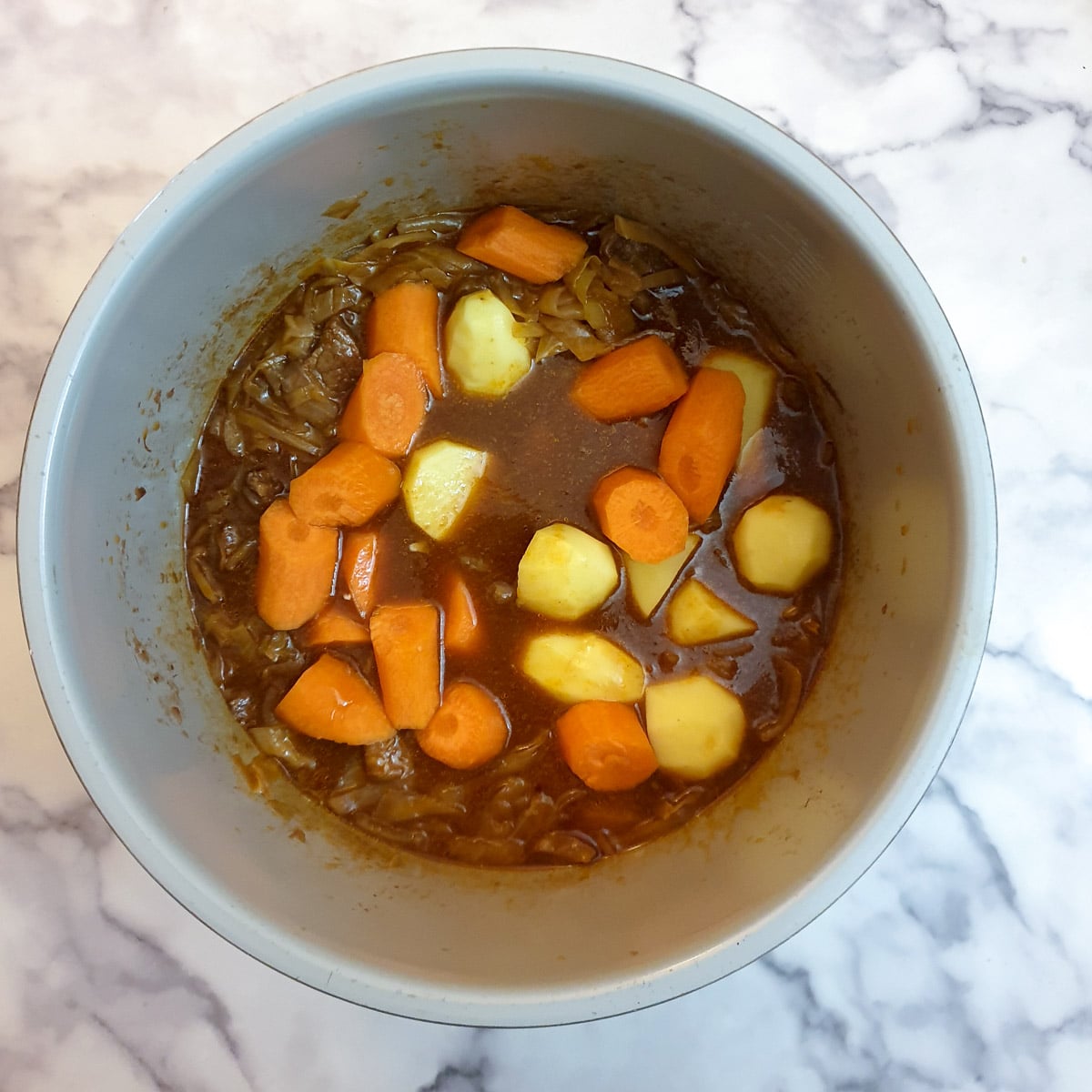 Raw potatoes and carrots being addd to the beef bredie.