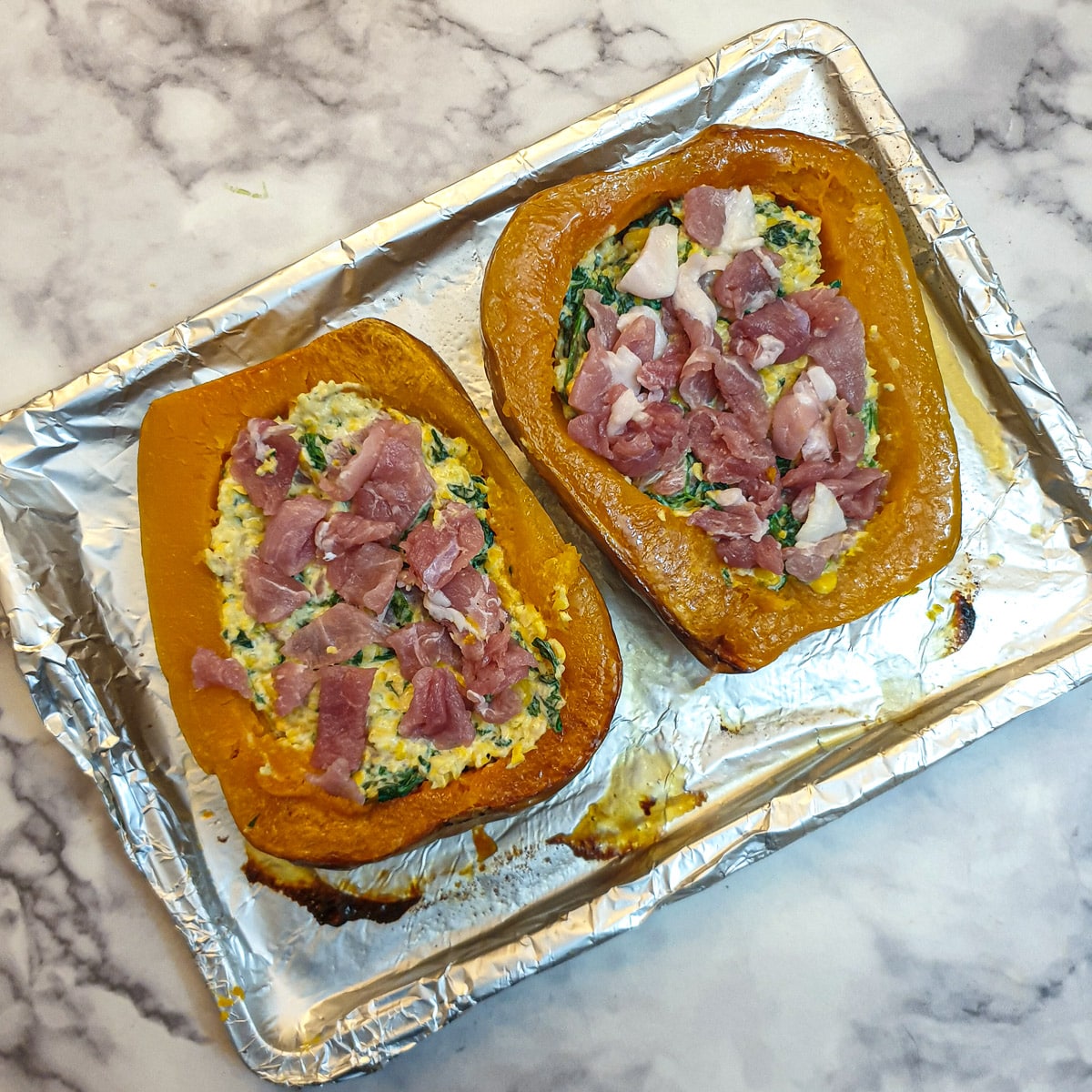 Two halved stuffed butternut squash on a baking tray ready to go into the oven.