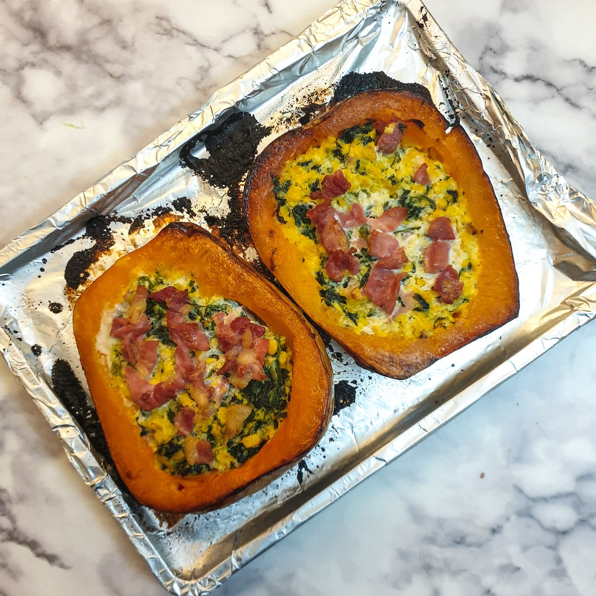 Two halved stuffed butternut squash on a baking tray after being baked in the oven.
