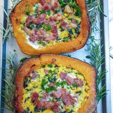 Overhead shot of 2 roasted stuffed butternuts on a baking tray garnished with rosemary.