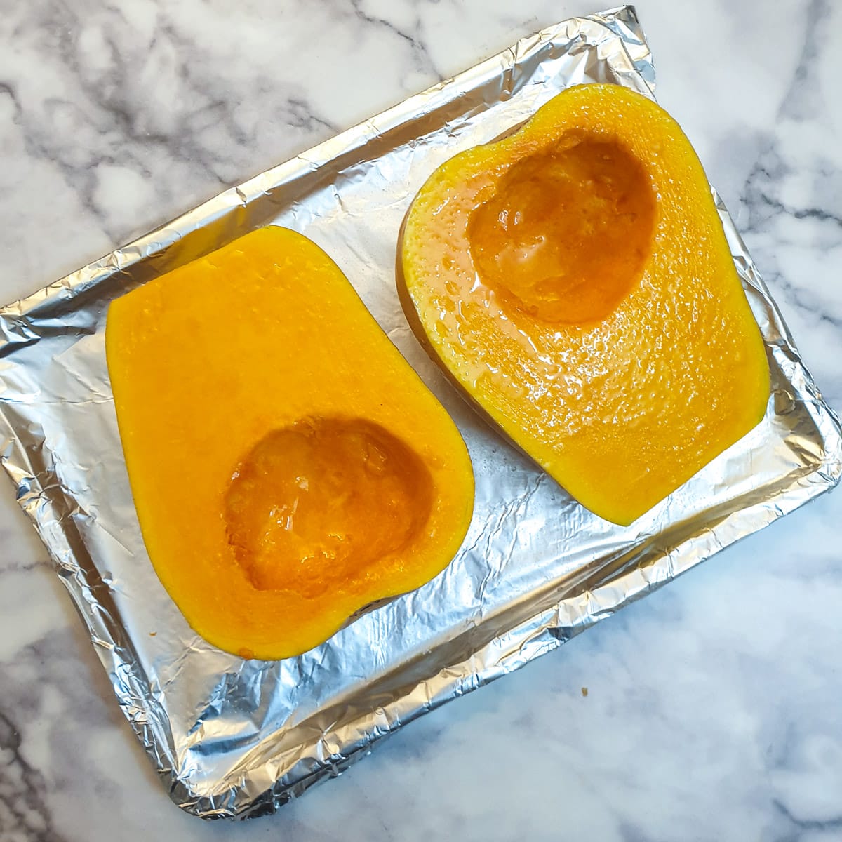 Two halved, cleaned butternuts, brushed with oil and salt, on a baking tray lined with tin foil.