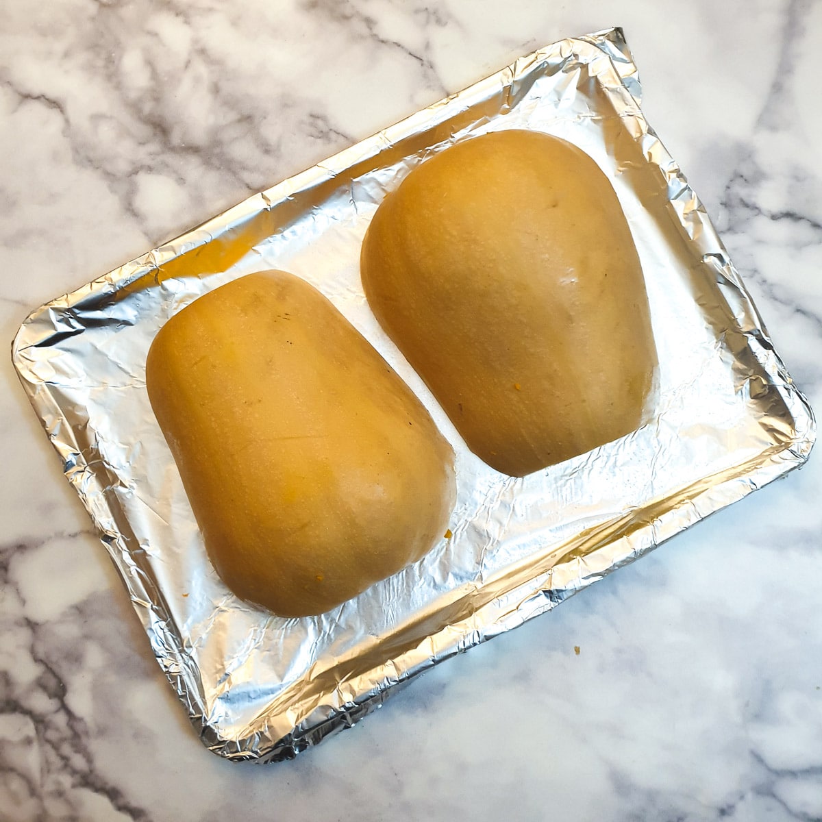 Two unbaked butternuts turned upside down on a baking tray.