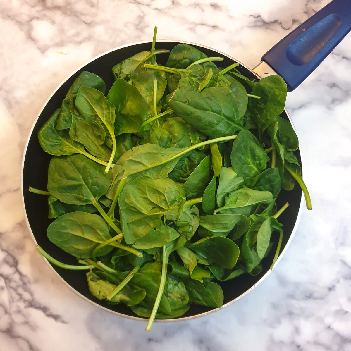 A large pile of raw baby spinach leaves in a frying pan.