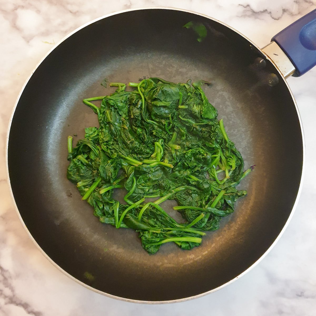 A small pile of wilted spinach in a frying pan.