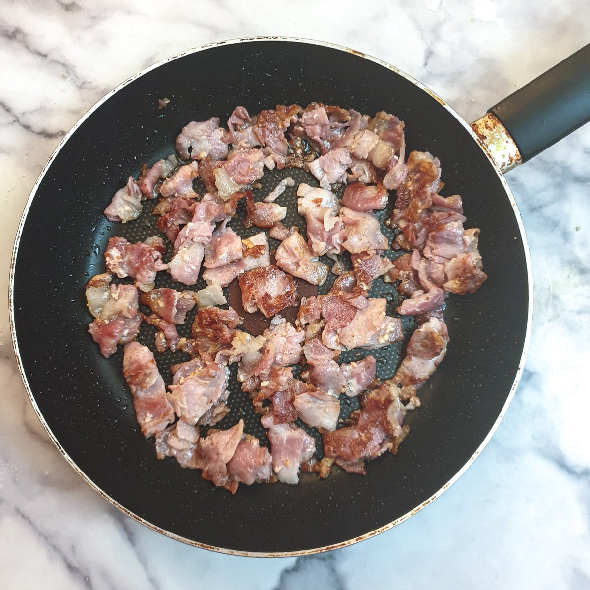 Chopped bacon frying in a pan.