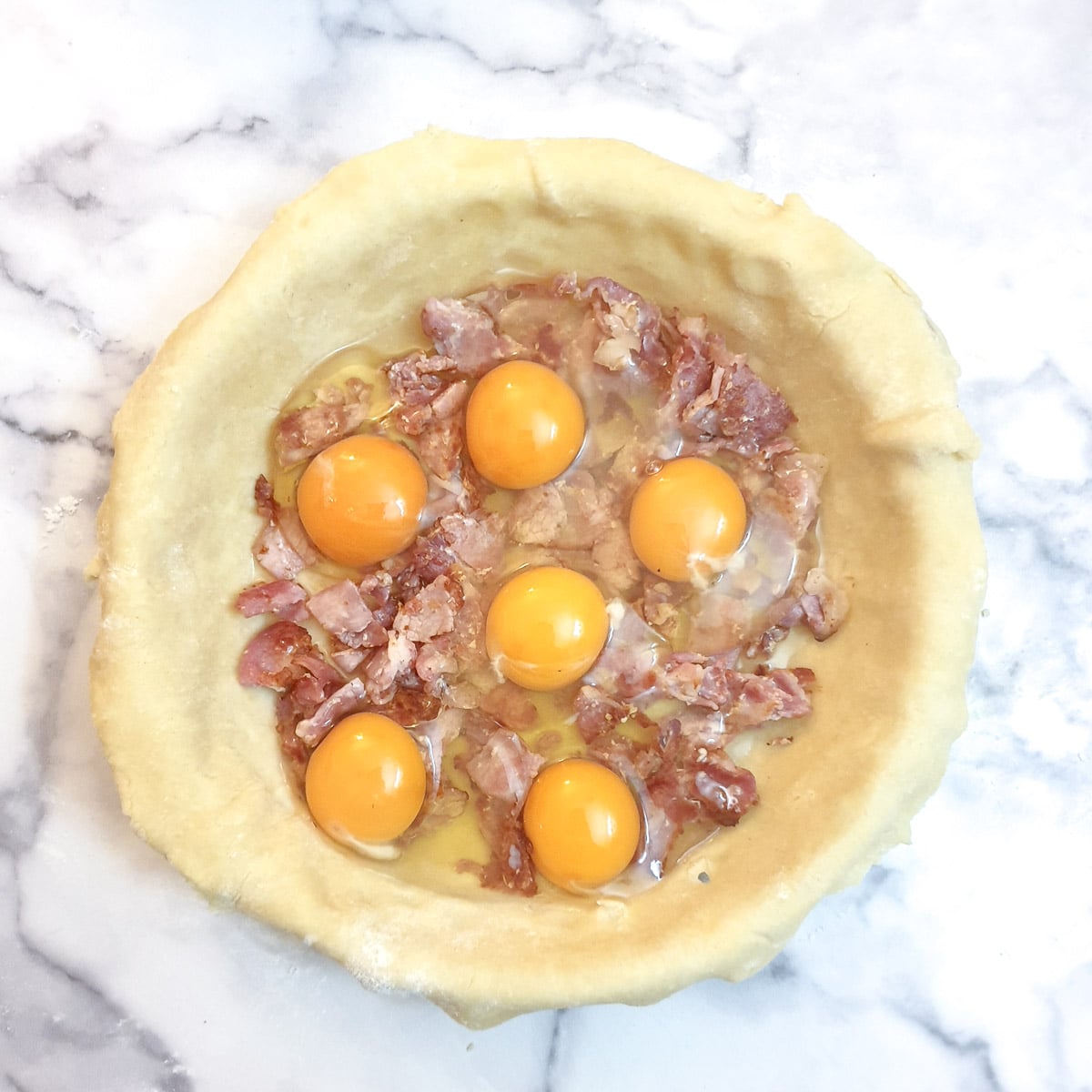 Raw eggs on top of bacon in a pie dish.