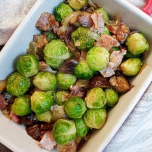 A white serving dish filled with brussels sprouts with chestnuts and bacon.