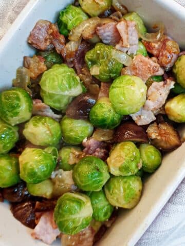 A white serving dish filled with brussels sprouts with chestnuts and bacon.