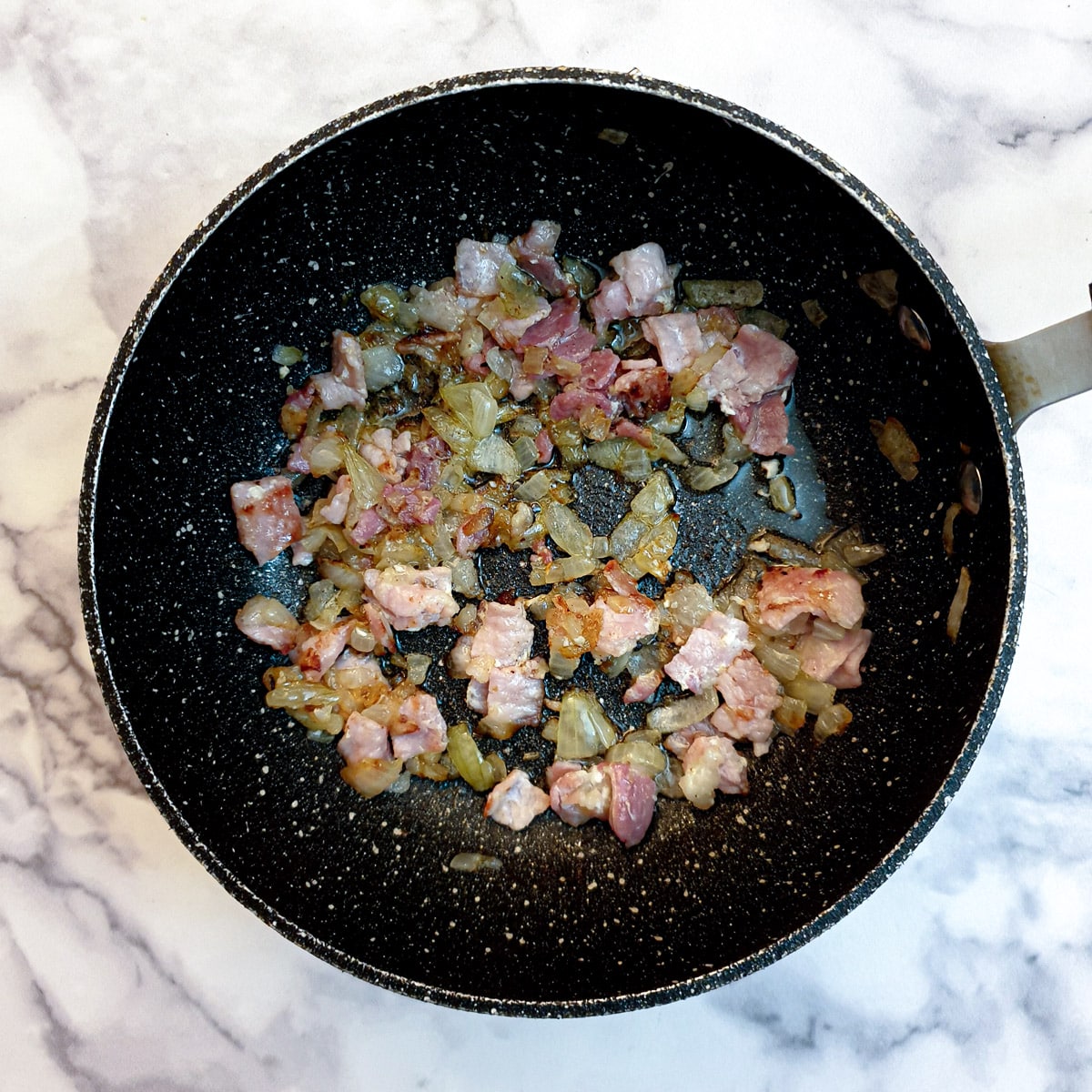 Chopped bacon and onions frying in a black pan.