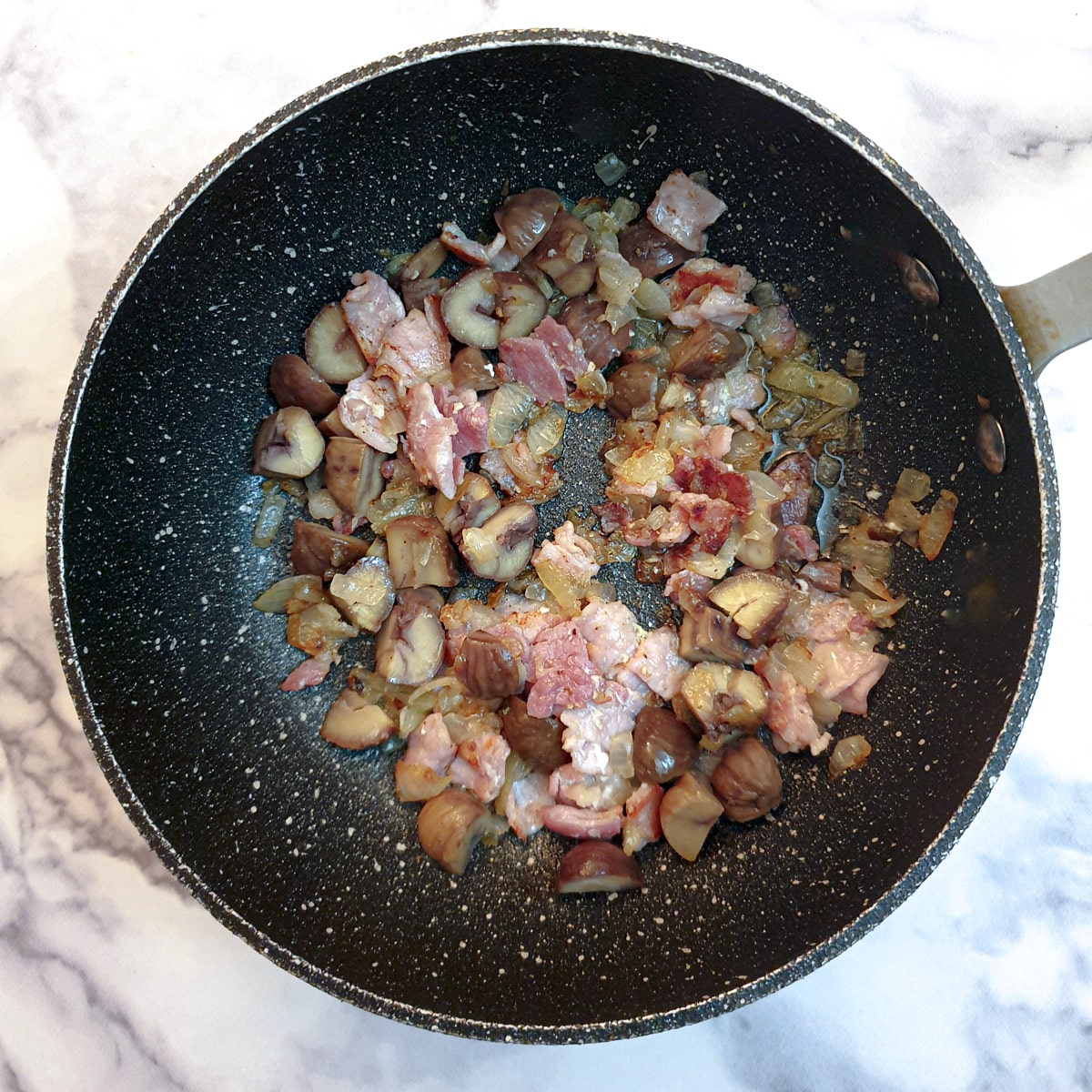 Chestnuts with bacon and onions in a black pan.