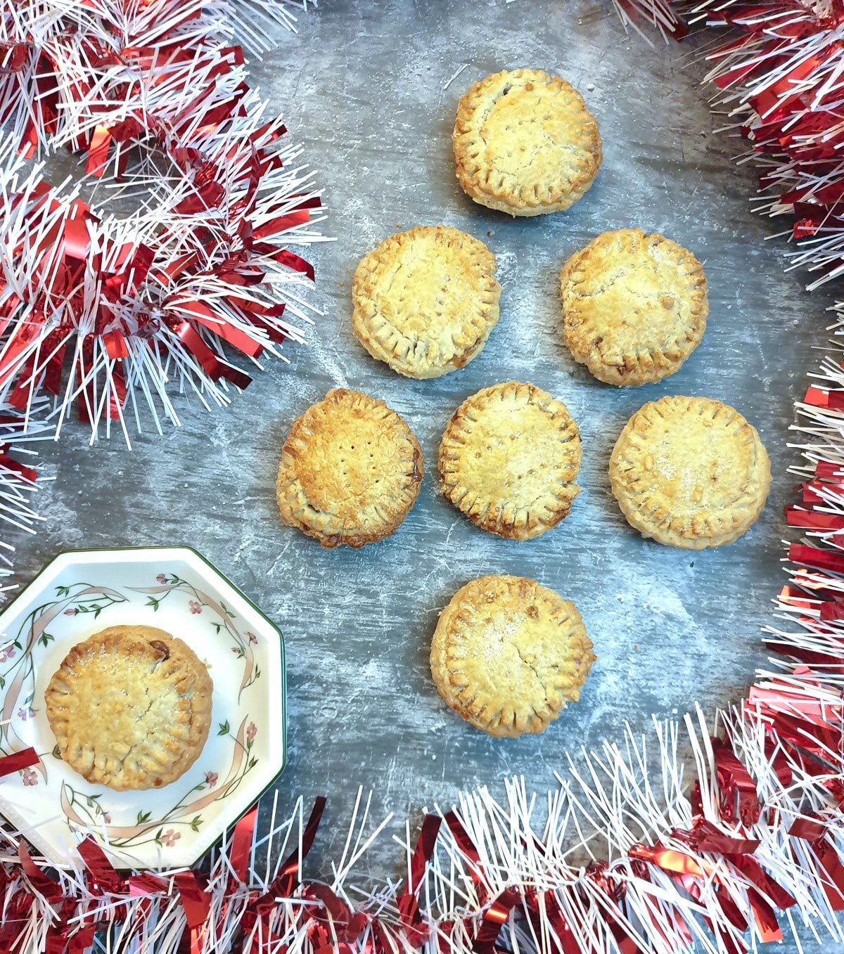 Mince pies arranged in the shape of a Christmas tree on a table surrounded by red and silver tinsel.