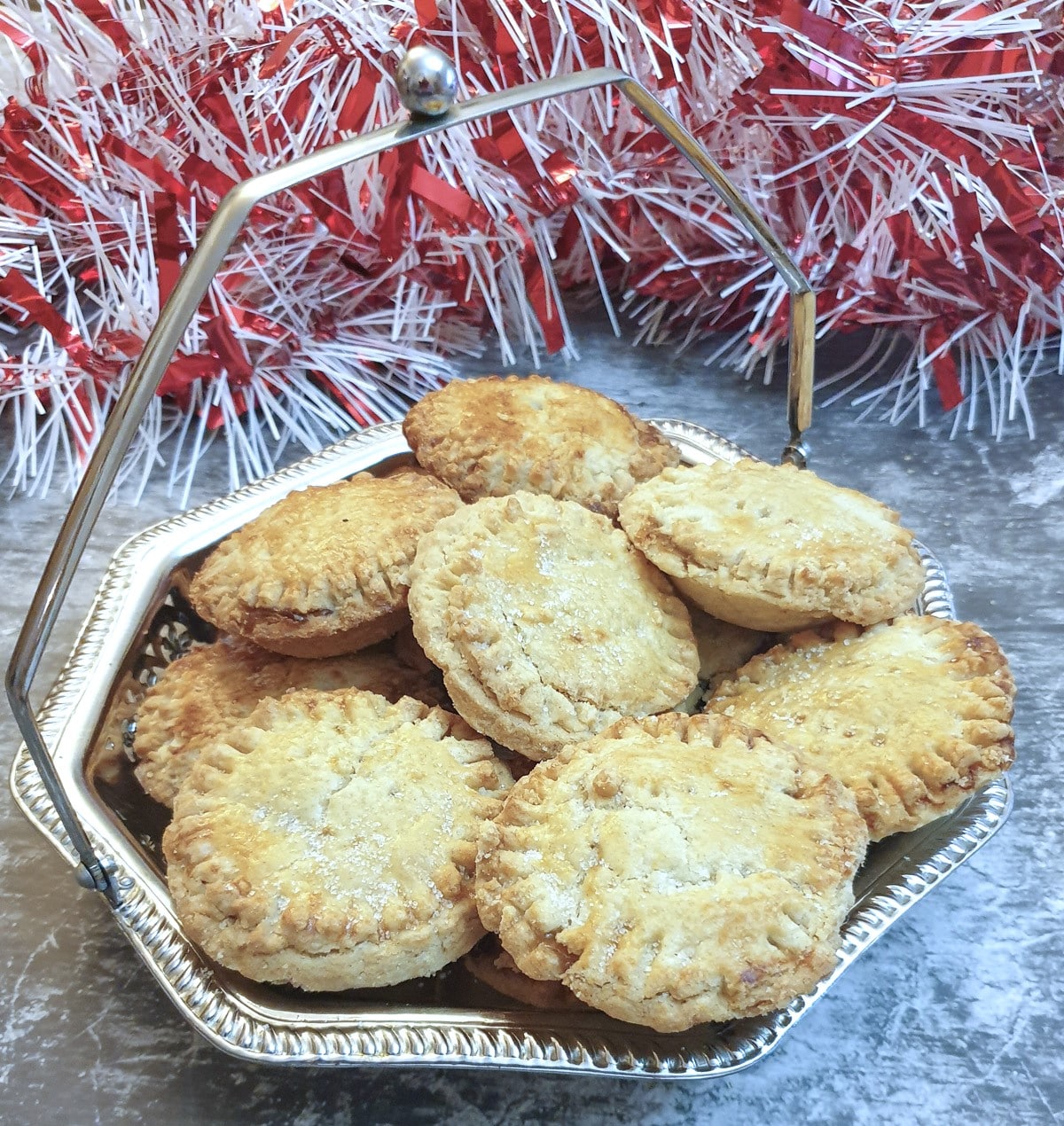 A silver dish of Christmas mince pies in front of a pile of red and white tinsel.