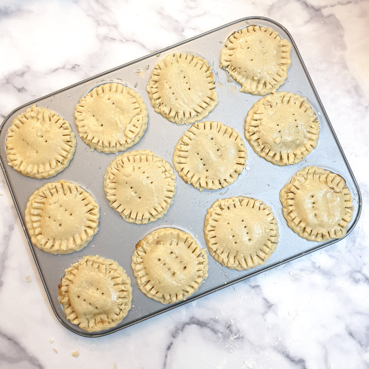 12 assembled but unbaked Christmas mince pies in a jam-tart tin.