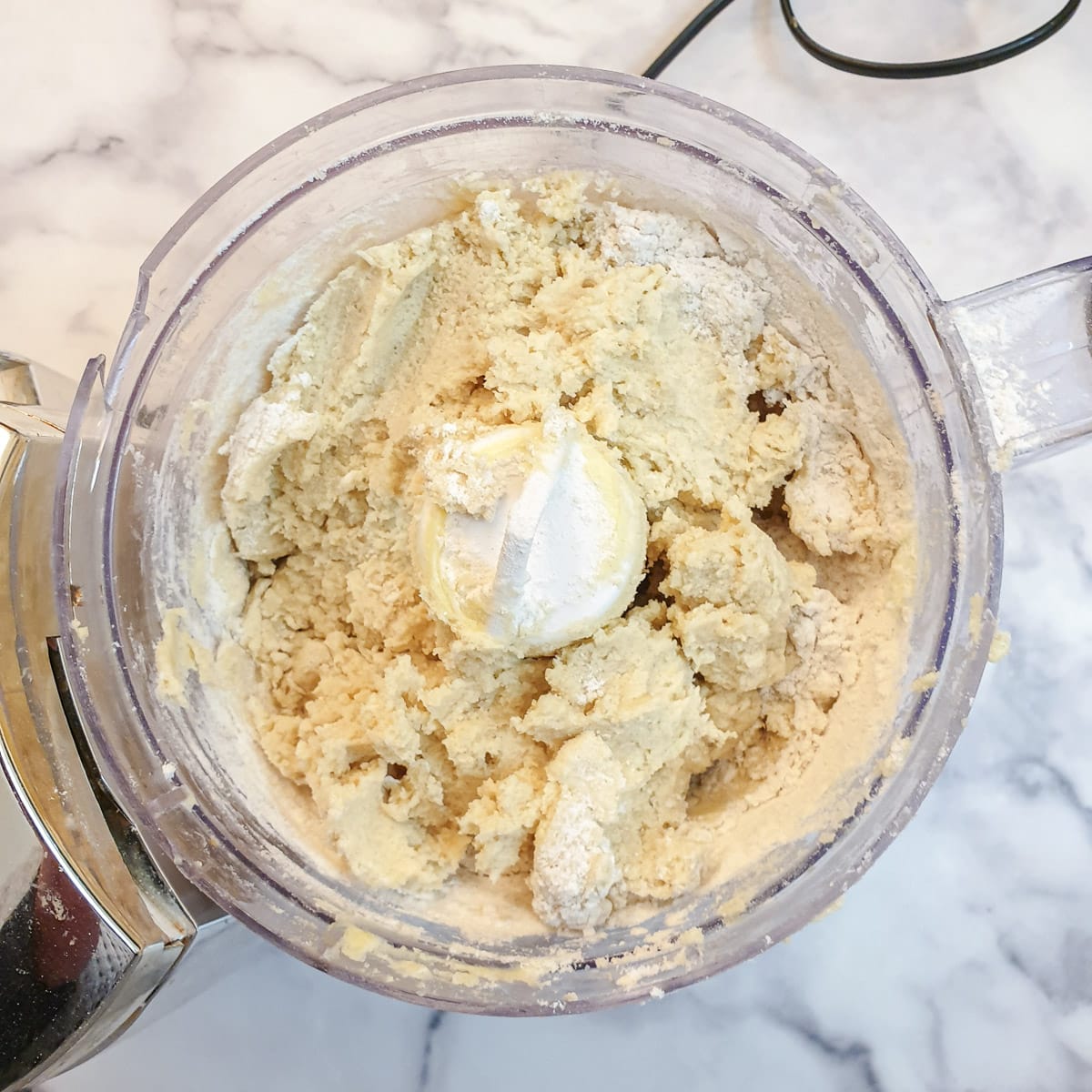 A shaggy dough in the bowl of a food processor.