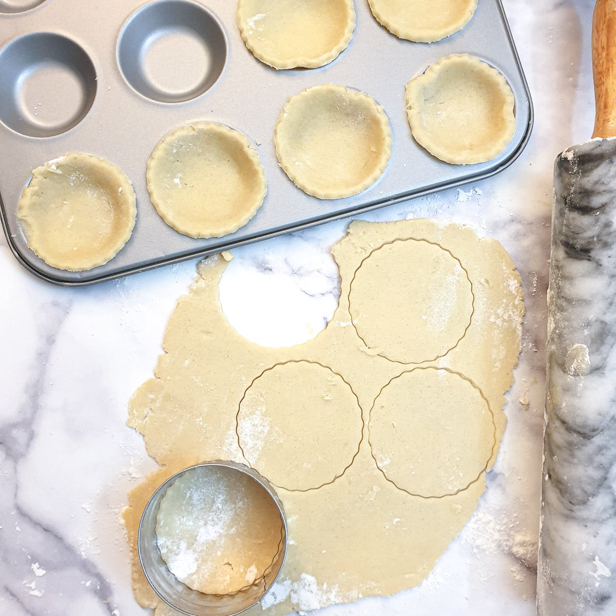 Rolled pastry being cut to shape and used to line a 12-hole jam tart tin.