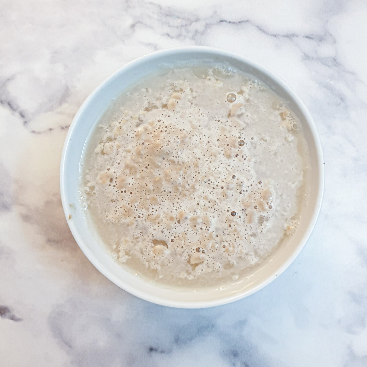 Yeast and water foaming in a small white bowl.