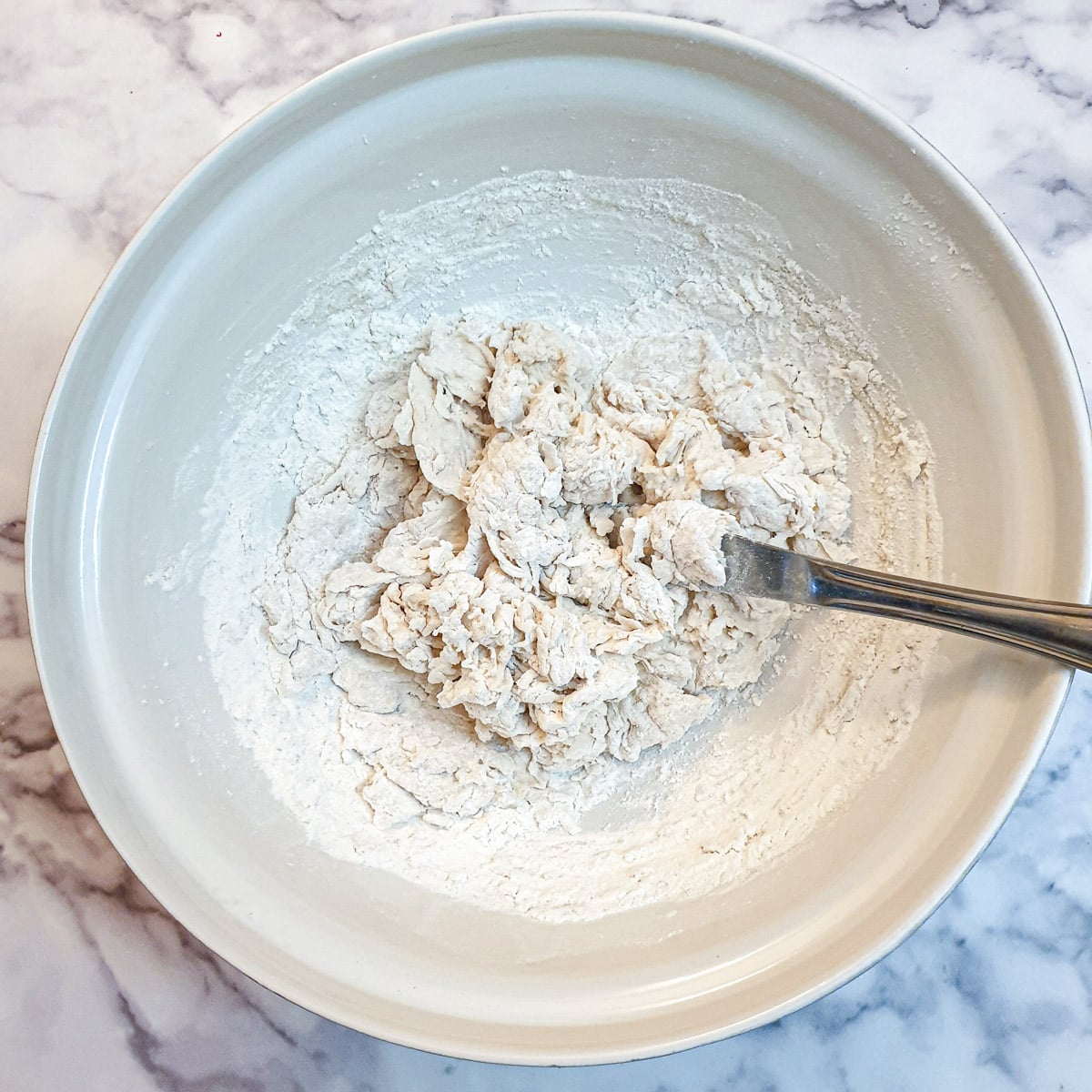 Focaccia dough being mixed with a flat-bladed knife to form a shaggy ball of dough.