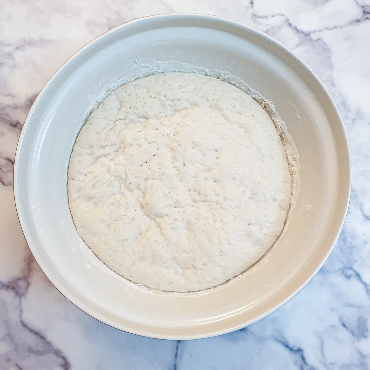 Focaccia dough that has been allowed to rise in a large mixing bowl.
