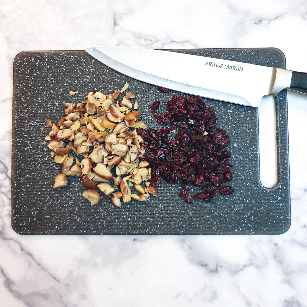 Cranberries and chestnuts being chopped on a blue chopping board with a knife.