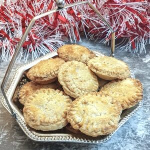 A silver dish of Christmas mince pies in front of a pile of red and white tinsel.
