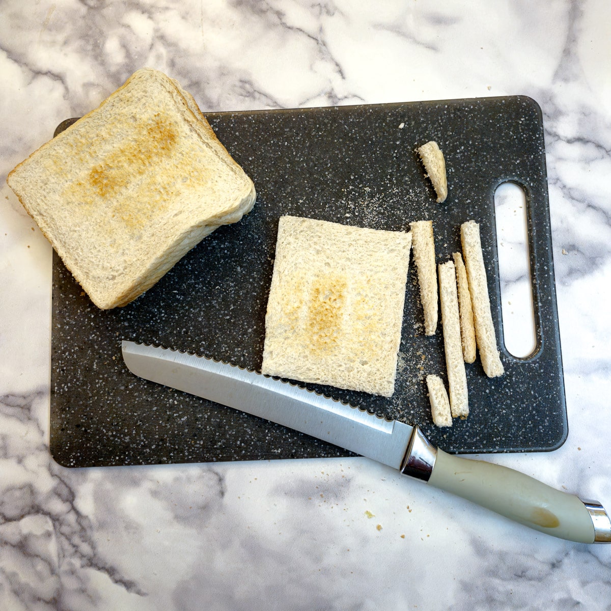 Slices of toast on a chopping board with the crusts removed. A bread knife is in the foreground.