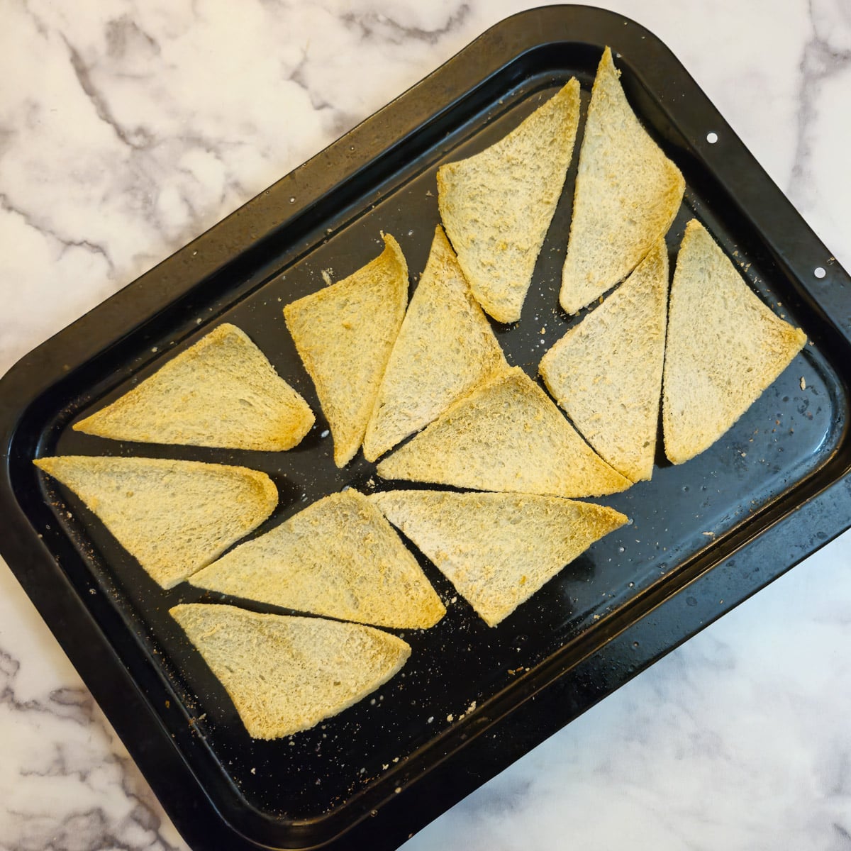 Light golden brown toasted melba toast triangles on a baking sheet.