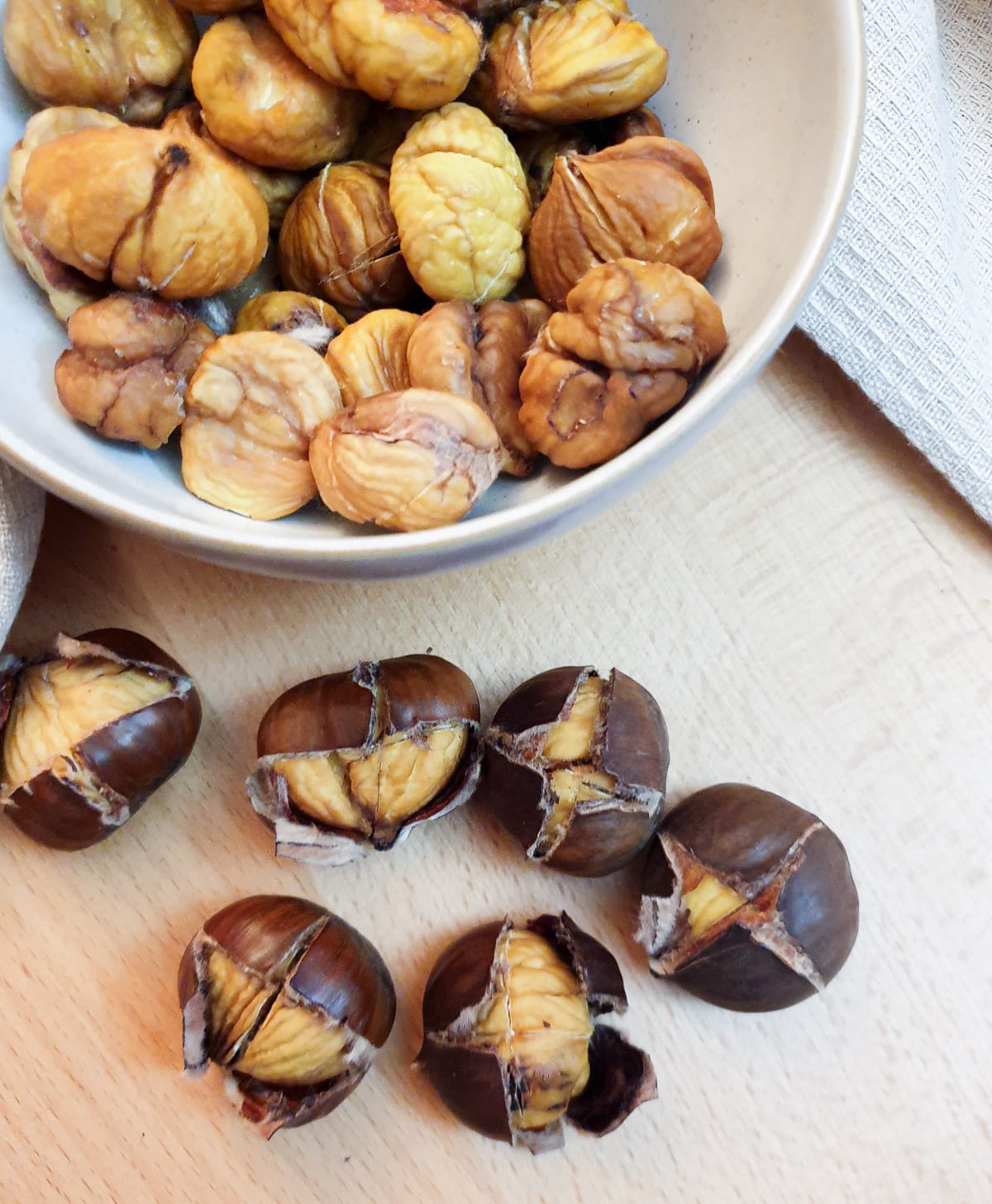 A dish of peeled roast chestnuts with 6 unpeeled roasted chestnuts in the foreground.