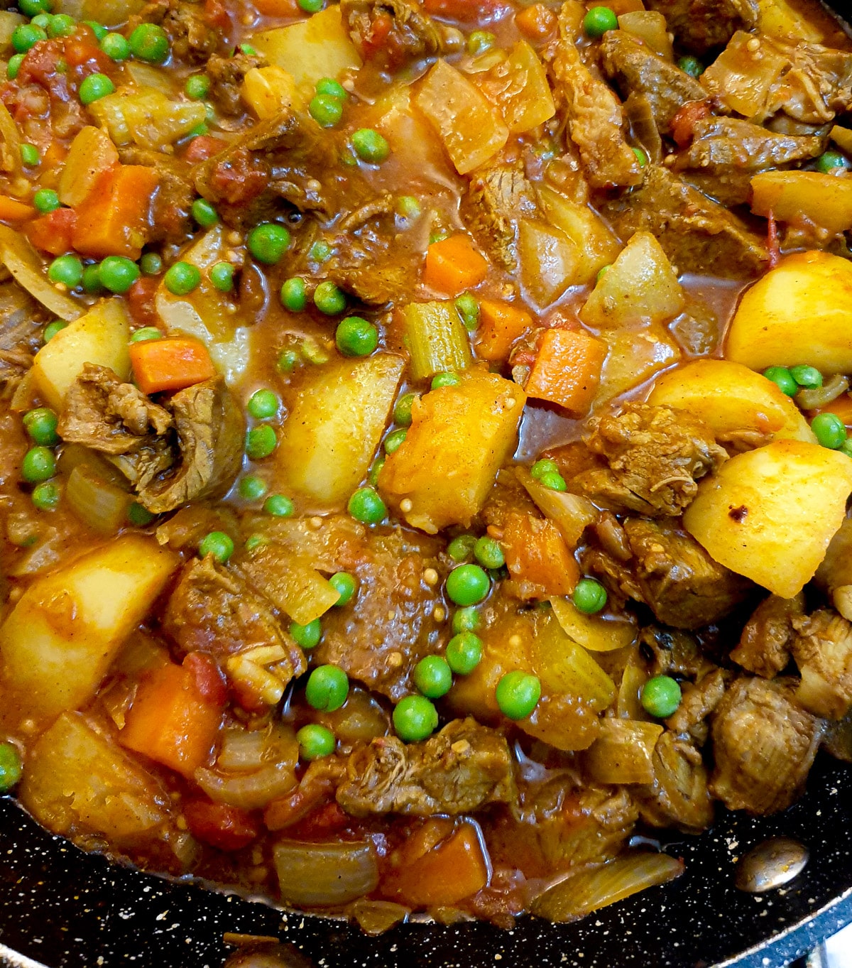Close up of leftover lamb curry with potatoes, peas and other vegetables.