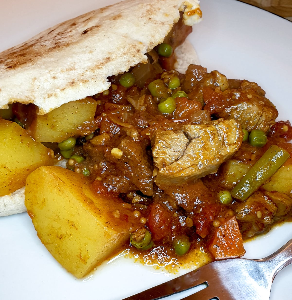 Leftover lamb curry in pita bread on a white plate.