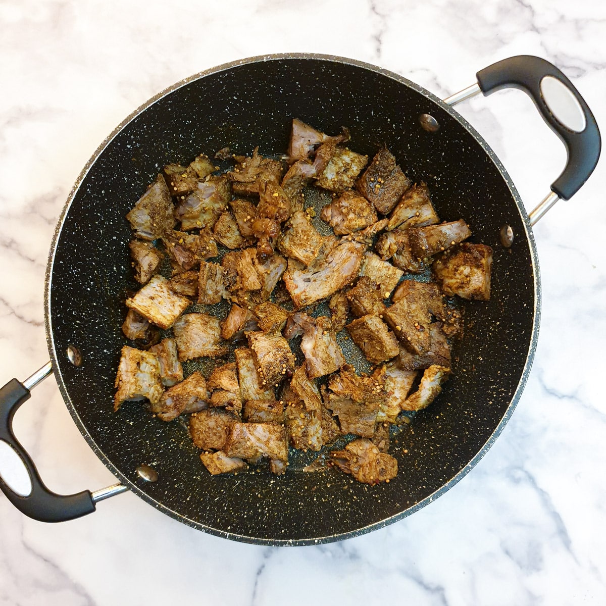 Cubes of lamb coated with spices in a frying pan.