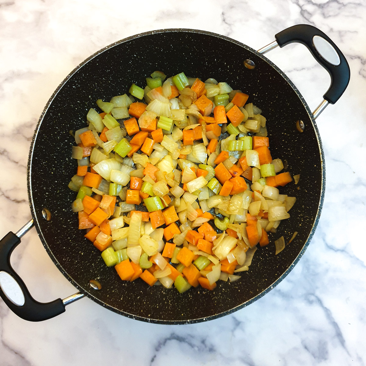 Carrots, onions and celery pieces frying in a frying pan.