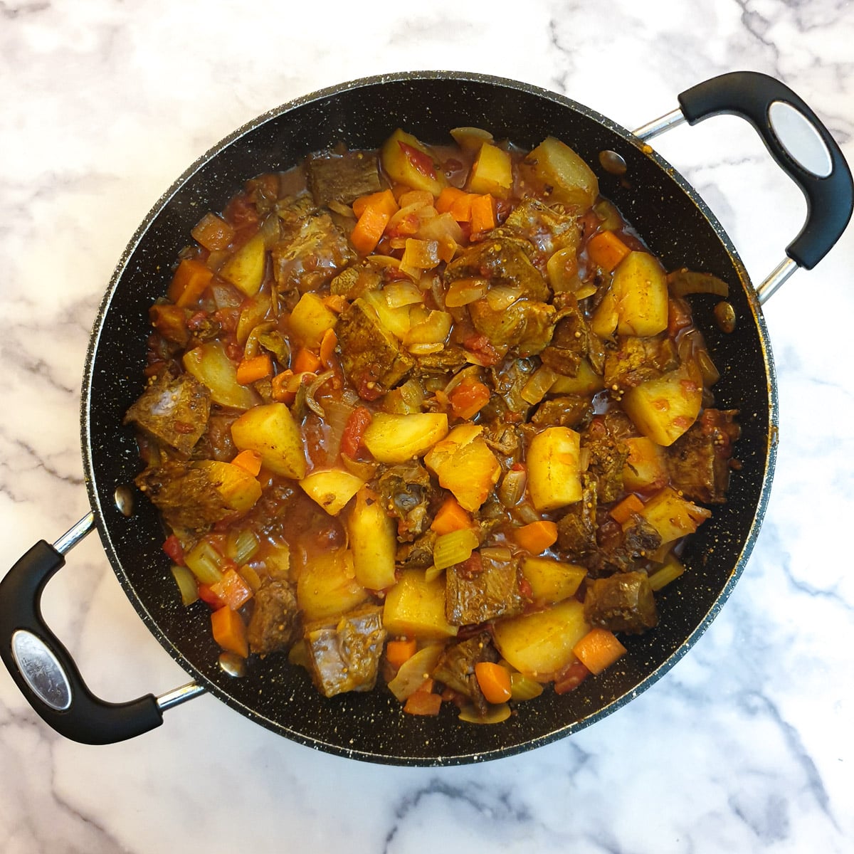 Cubed lamb added to cuirry sauce in a frying pan.