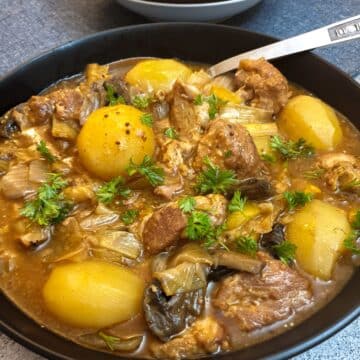 Close up of a black serving bowl filled with potatoes and pork casserole.