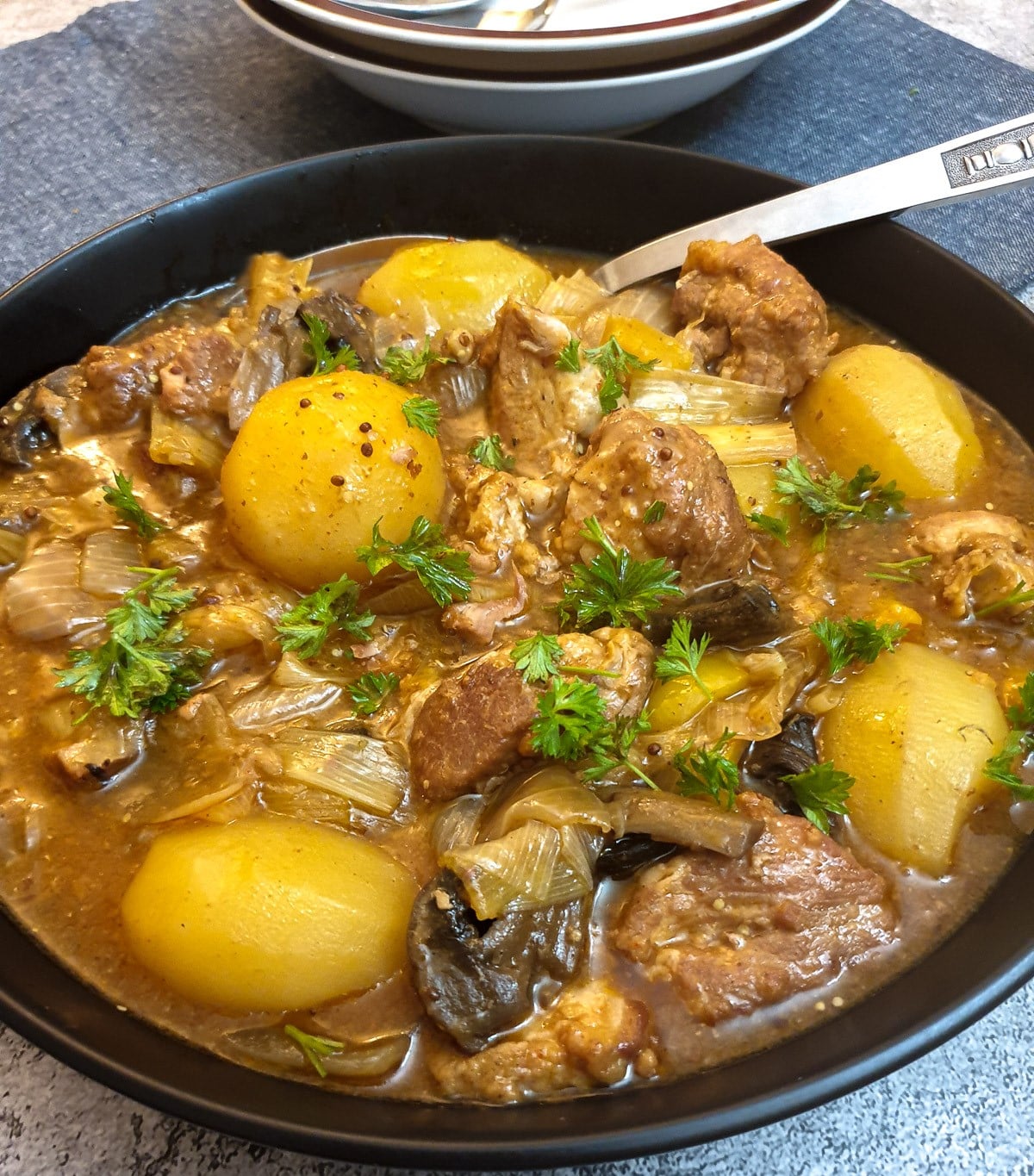 Close up of a black serving bowl filled with potatoes and pork casserole.