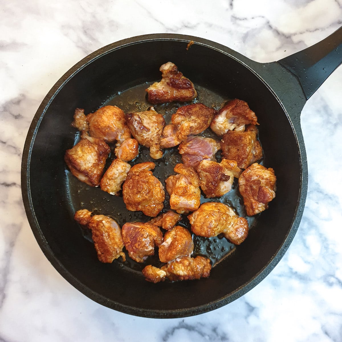 Flour-coated pieces of pork browning in a frying pan.