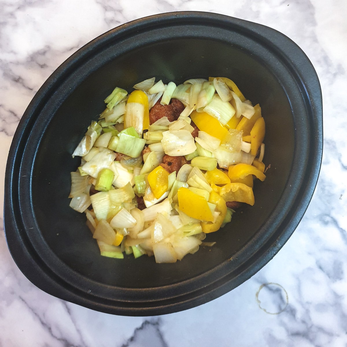 Chopped onions, leeks and yellow pepper with pieces of pork in a slow-cooker.