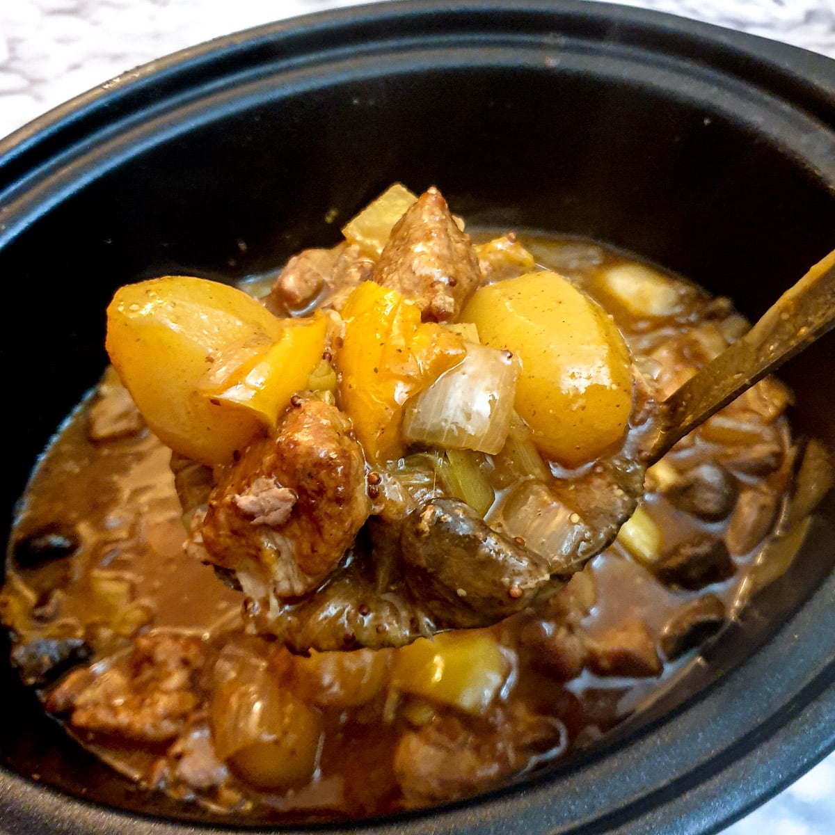 A spoonful of cooked pork casserole held above a slow-cooker.