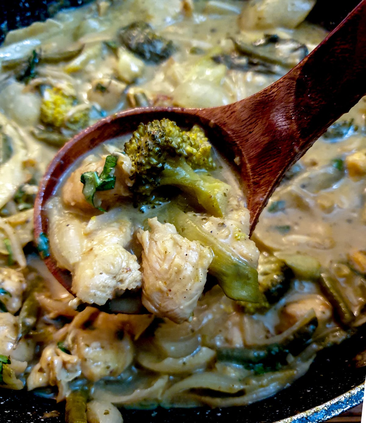 A large wooden spoon lifting Thai green curry from a serving dish.