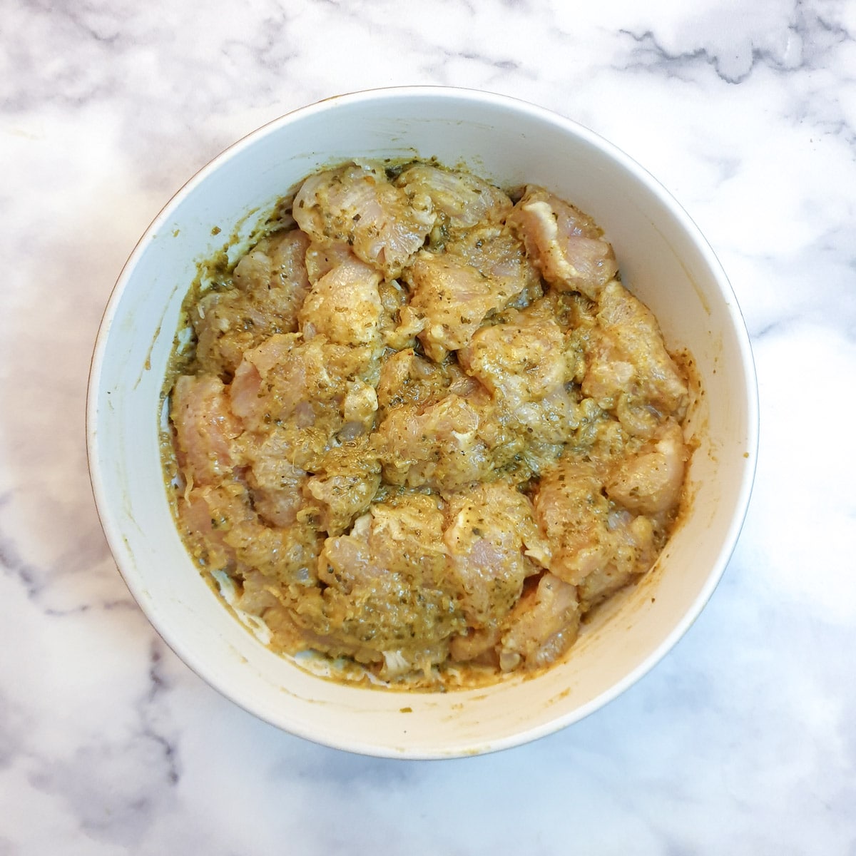 Chicken pieces in a Thai green curry marinade in a small white bowl.