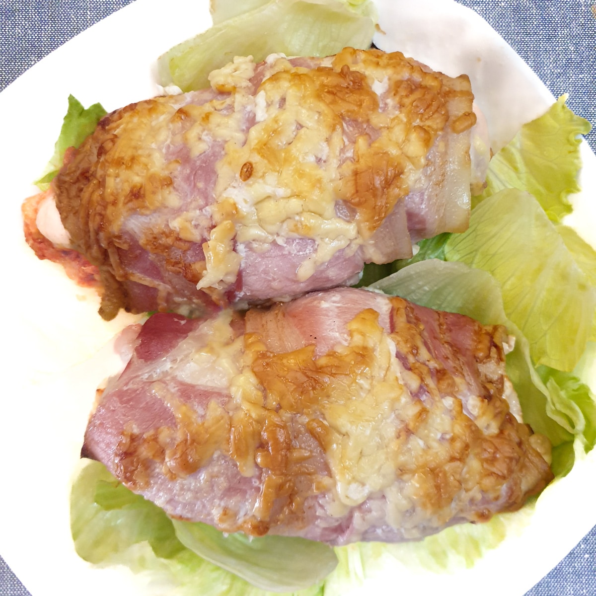 Two bacon wrapped chicken breasts on a bed of lettuce on a white plate.