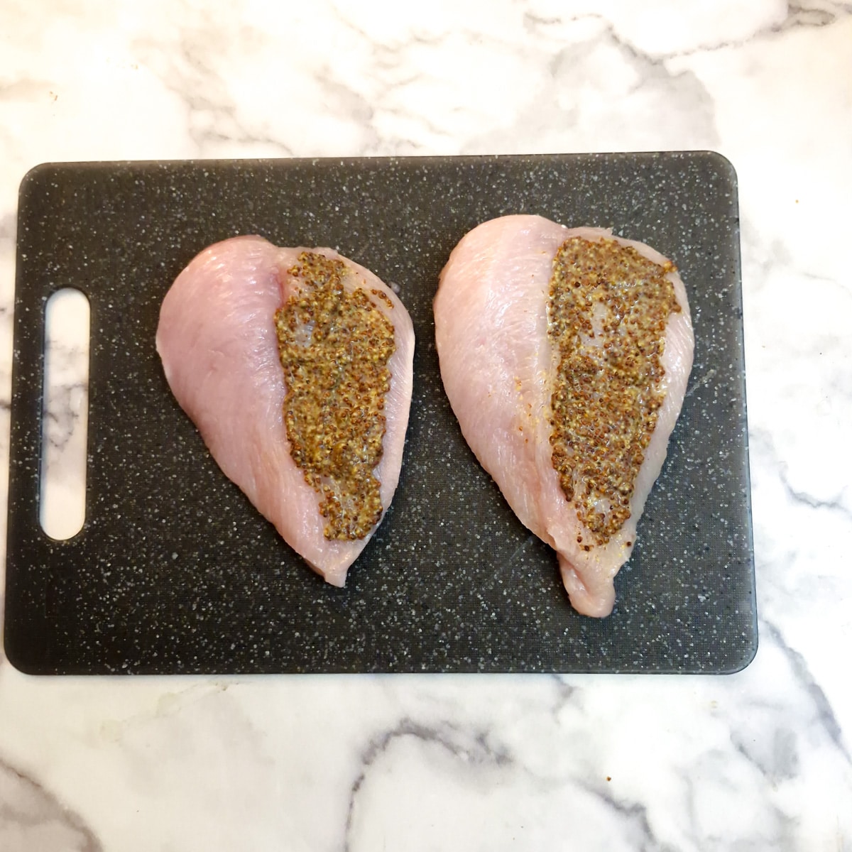 Two butterflied chicken breasts each with mustard spread on one side.